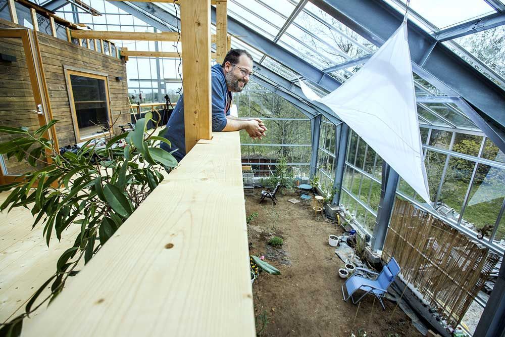 Mann står på balkongen til huset sitt, som er inni et drivhus