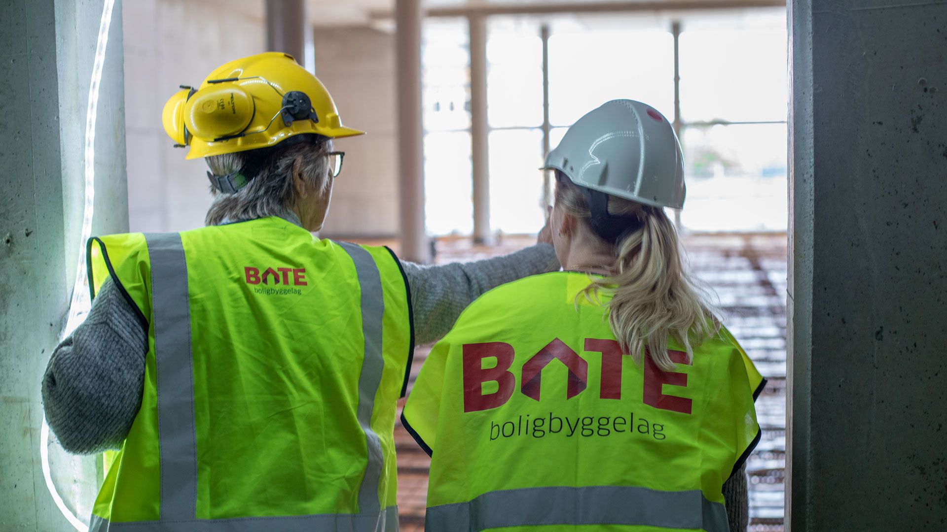 To damer på befaring i tomme butikklokaler ikledd vernetøy